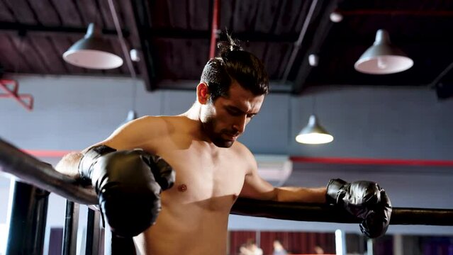 Young athlete who specializes in boxing, leaning against long string on boxing ring exhausted during sparring time, man breathing heavily, in mouth wear boxer teeth prevent broken teeth.
