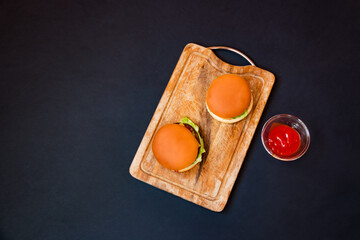 Two burgers and tomato ketchup on cutting board. Top view, copy space.
