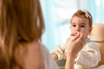 Young mom feeding her baby daughter with a spoon