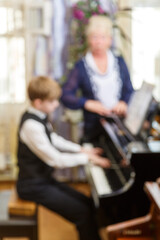 The boy plays the piano under the guidance of a teacher.