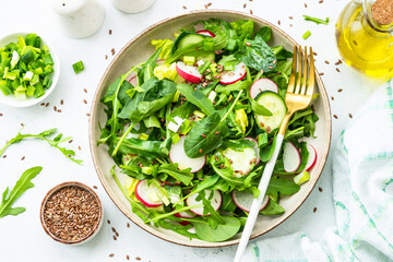 Green salad with spinach, arugula and radish with olive oil. Top view on white.