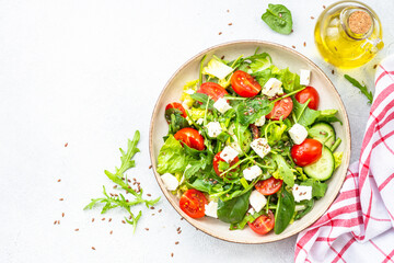 Spring salad in craft plate. Spinach, arugula, tomatoes and feta with olive oil. Top view on white.