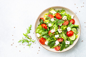 Green salad with spinach, arugula and tomatoes with olive oil. Top view on white.