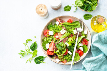 Healthy salad with green leaves, tomatoes and jamon. Top view in craft plate.