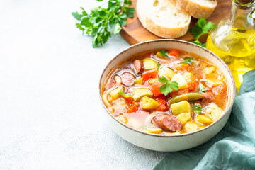 Minestrone soup, italian vegetable soup with smoked sausages, Top view on white table.