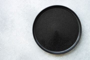 Black plate on white stone table. Empty plate top view.