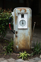 Eine alte Kraftstoffzapfs&auml;ule, in der N&auml;he einer Ansammlung &uuml;ppiger gr&uuml;ner Bl&auml;tter, die einen auff&auml;lligen Kontrast bildet