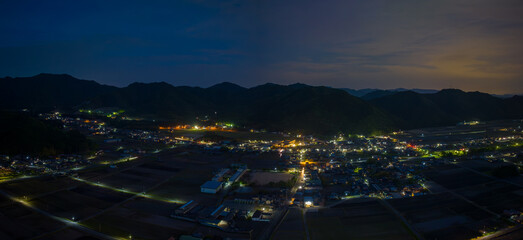 Panoramic aerial view of lights from small town at foot of mountain range at night - 604378754