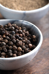 Black peppercorns (Black pepper) in a bowl on a wooden background.