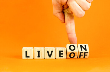 Live on or off symbol. Businessman turns wooden cubes and changes word Live off to Live on. Beautiful orange table orange background. Business and live on or off concept. Copy space.