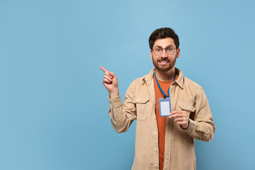 Fototapeta premium Smiling man showing VIP pass badge on light blue background, space for text