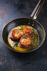 Traditional roasted veal filet medallions with bacon coating and sage leaves in butter sauce served as close-up on a rustic wrought iron skillet