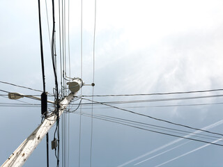 A wooden electric pole against a blue cloudy sky. You can see various cables and wires diverging from the pole. There is free space and empty place for the placement of various elements.