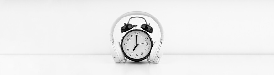 Black alarm clock with headphones on white wall background