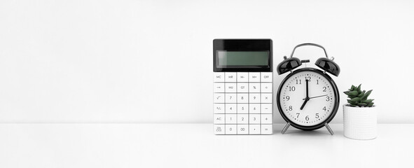Black alarm clock with calculator against a white wall. Financial concept.