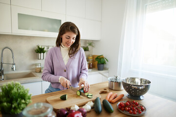 Woman chopping cucumber on the wooden board in the kitchen