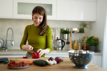 Woman chopping red bell pepper on the wooden board in the kitchen