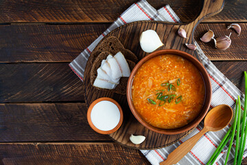 Cabbage soup in bowl with green onion, bread and salo on wooden background. Top view