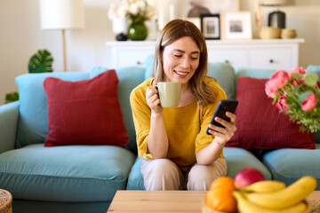 Woman using smartphone while drinking coffee at her home in the morning