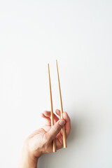 Right hand holding wooden chopsticks, ready for using, isolated on white, vertical frame, bottom to top, view from above