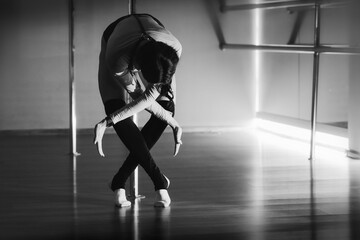 A female person dances in a pole dance hall. Horizontal black and white photo with motion blur...