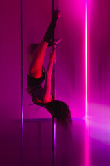 A beautiful girl in neon red light hangs upside down from a pole in a dancesport gym. Motion blur effect for dynamic effect.