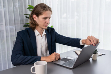 Businessman in black suit working on laptop at his workspace desk. Smart executive researching financial data and planning marketing strategy on corporate laptop at modern workplace. Entity