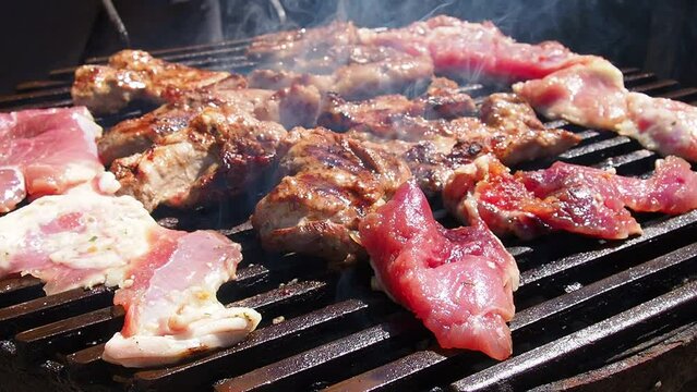 Grilled juicy meat pork steaks in burning coals on a barbecue grill, flames and smoke. Barbecue grill. Grilled cooked and raw pieces of meat are laid out on a grill grate