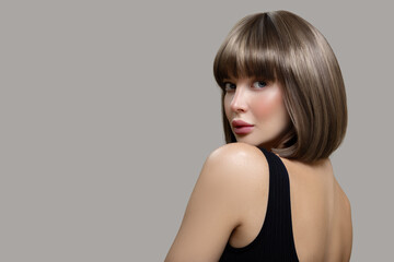 Portrait of a beautiful brown-haired woman holding with shiny short hair. Gray background.