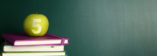 Apple with carved number five as school grade on books near green chalkboard. Banner design with space for text