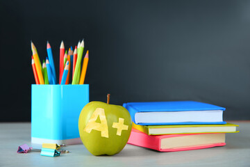 Apple with carved letter A and plus symbol as grade. School stationery on white table in classroom,...