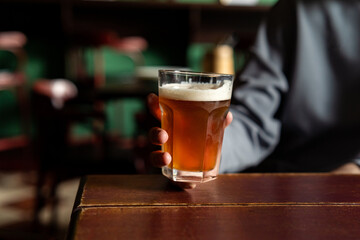 Unrecognizable person holding glass with cold beer in the bar
