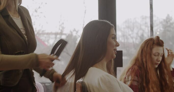 Hairstylist combing long hair of customer in hairstyling studio, trucking motion