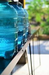 A row of large bottles of drinking water cooler put on the brown wood table. Selective focus, vertical image.