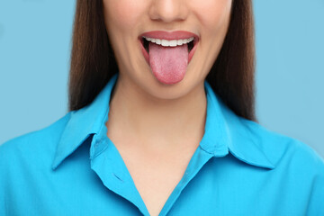 Obraz na płótnie Canvas Woman showing her tongue on light blue background, closeup