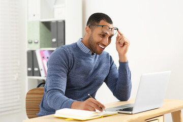 Smiling African American man writing in notebook at wooden table