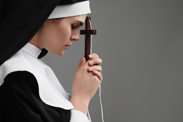 Nun with cross praying to God on grey background. Space for text