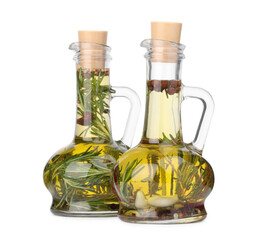 Glass jugs of cooking oils with spices and herbs on white background