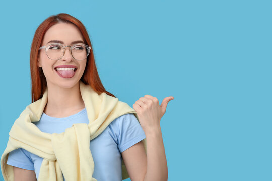 Happy woman showing her tongue and pointing at something on light blue background. Space for text