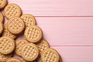 Tasty sandwich cookies with cream on pink wooden table, flat lay. Space for text