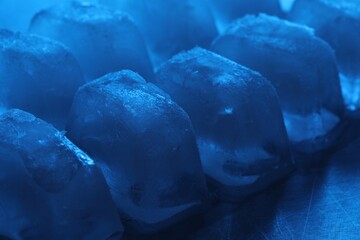 Crystal clear ice cubes on light blue background, closeup. Color tone effect