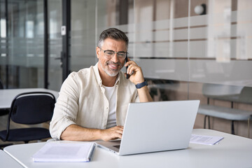Middle aged Latin or Indian businessman having call on smartphone with business partners or...