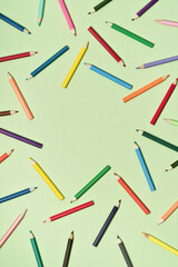Colored Pencils background pattern on light green. Back to School or drawing and creativity concept. Copy space in center. Top view