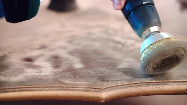 Carpenter using grinding machine with circle metal nozzle for sanding wooden board surface and removing old paint remnants. Craftsman polishing vintage wooden table in workshop, furniture renovation
