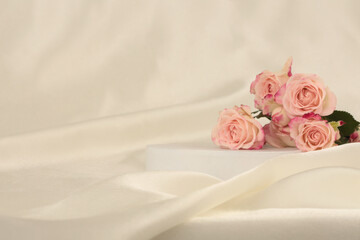 Pink rose flower bouquet on white podium and silk fabric.. Light beige background. Minimal empty...