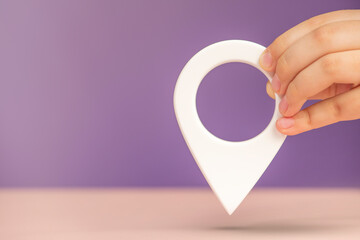 Pin icon or travel nautical map. GPS direction indicator. A hand holds a location sign on a purple background. Laying a route, finding a location. copy space.