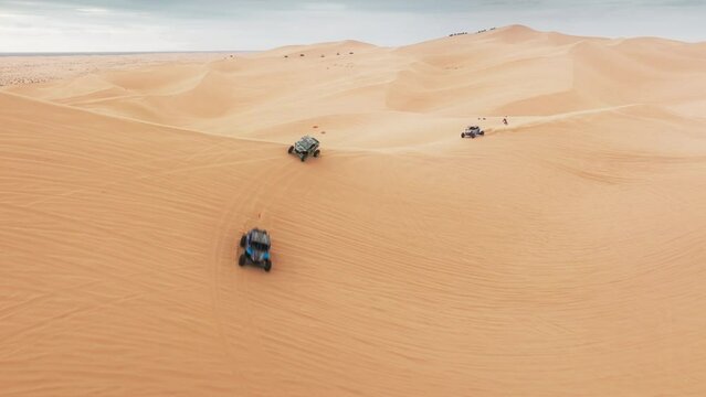 Group of four wheel drive vehicles competing on dunes. Aerial view of ATV buggy sport car riding fast by sand dunes. Extreme sport outdoor hobby on weekend day. Sport recreation concept for men 4K