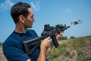 A man aims to shoot a rifle at a flying drone against a blue sky. 