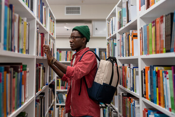 Interested Black student man choosing book for reading in bookstore. Focused young African American...