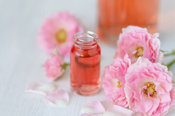 Composition with pure natural organic rose essential oil in glass bottle, luxury perfumery ingredient for premium fragrance, skin care products, anti-age beauty treatment. Fresh flowers